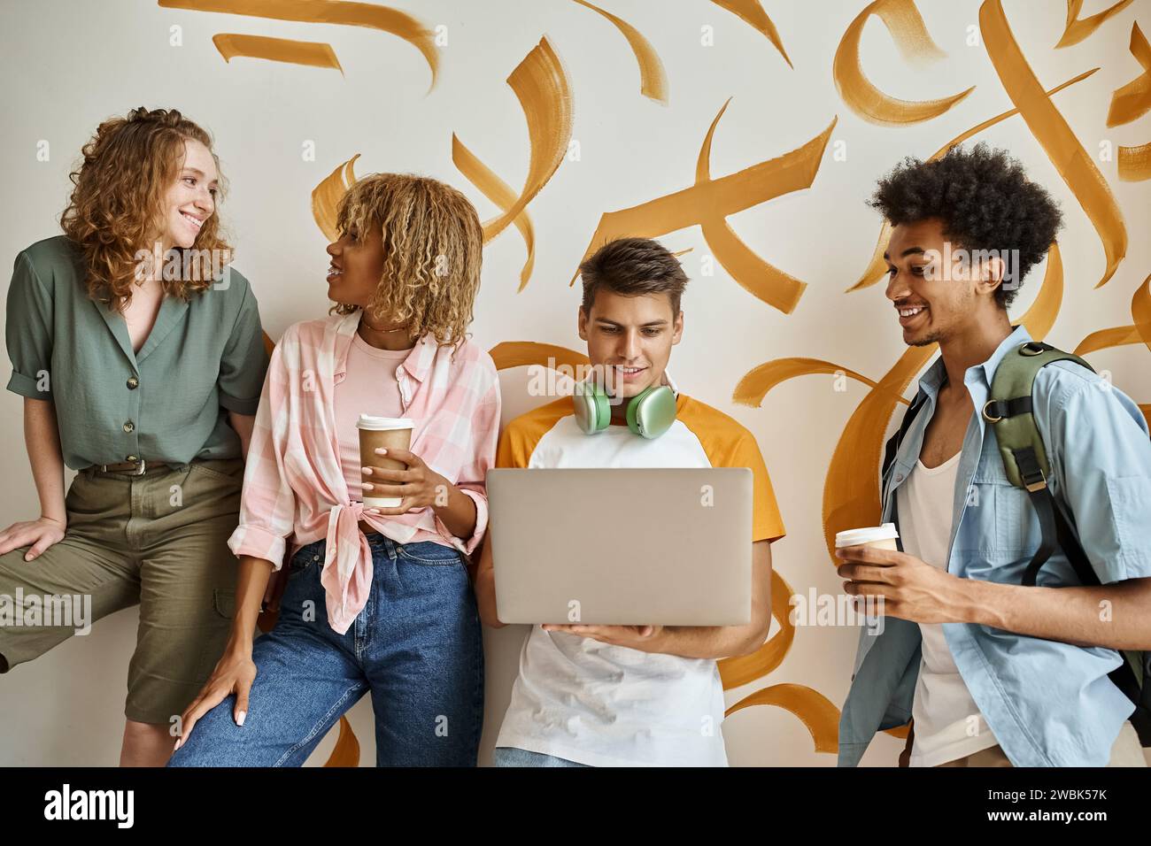 allievi multietnici con caffe' da portare via e portatile sulle scale dell'ostello con pareti colorate Foto Stock