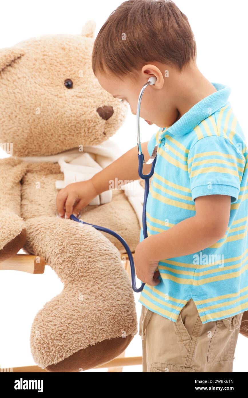 Bambino, orsacchiotto e stetoscopio in studio per giocare a medico, ascoltare e benessere su sfondo bianco. Kid, gioco sanitario e sviluppo Foto Stock