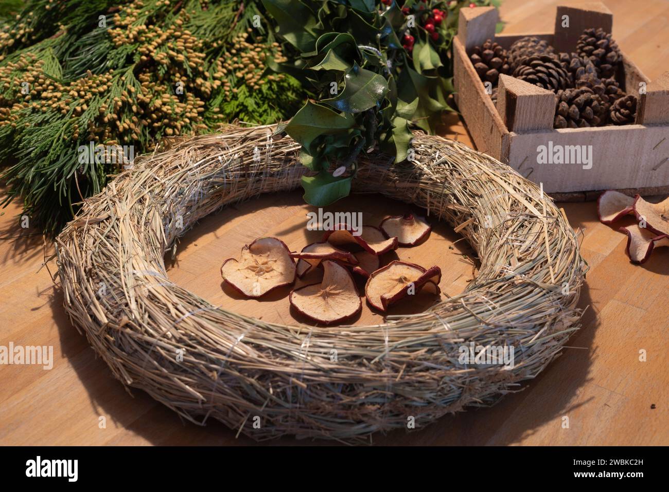 Una corona bianca, mele di pino e vegetazione di abete giacciono su un tavolo. Gli utensili vengono utilizzati per creare una corona dell'Avvento autolegata. Foto Stock