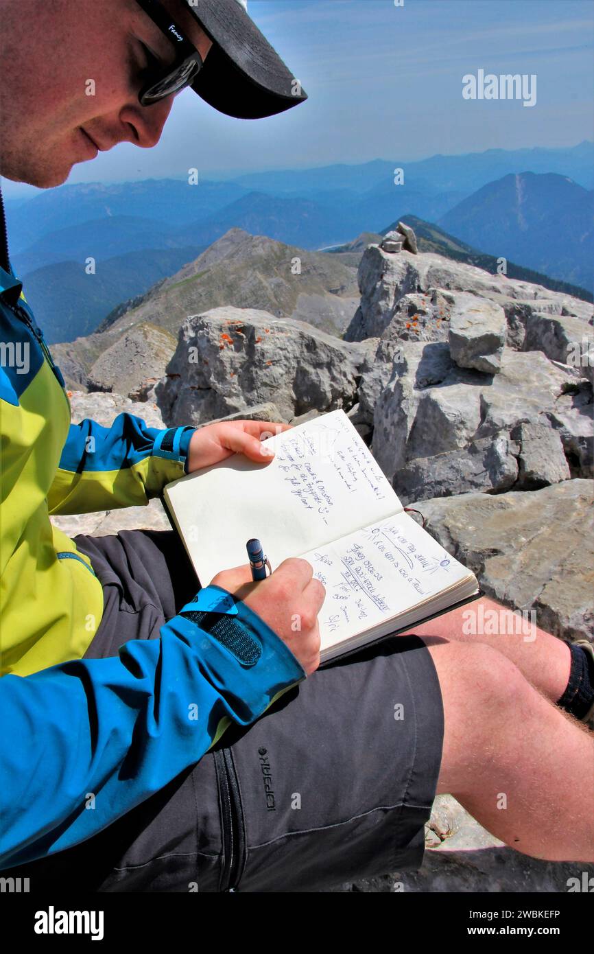 Escursione al Soiernspitze (2257 m), il giovane fa un'entrata nel libro sulla vetta, di fronte a un cielo blu brillante, Soierngruppe, Soiernberggruppe, Karwende Foto Stock