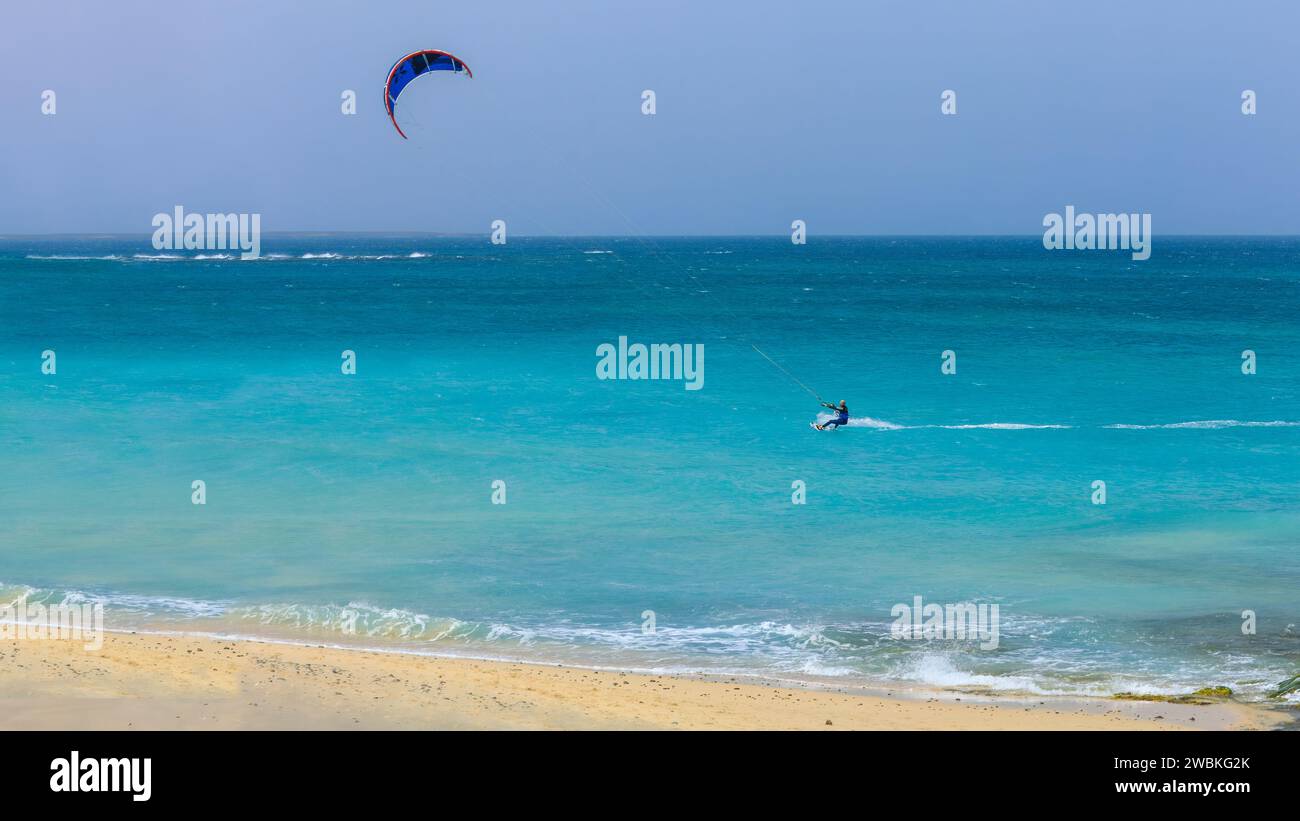 Un kitesurfer scivola sul mare turchese sulla costa sabbiosa di Boa Vista, godendosi il sole e l'emozione di questo sport. Foto di alta qualità Foto Stock