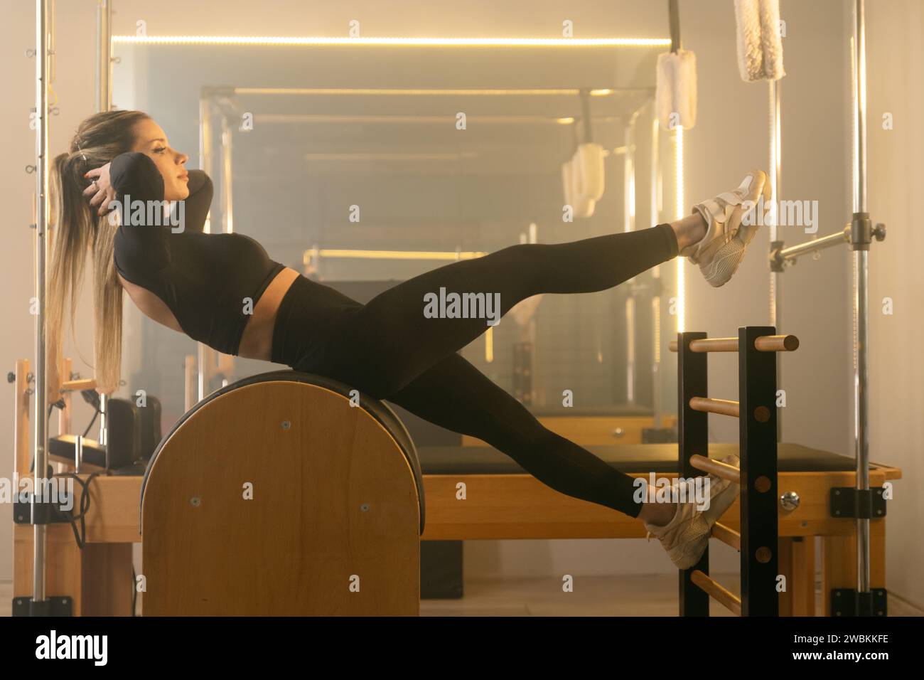 Foto di una giovane donna che fa esercizi di base su una macchina Reformer Pilates in palestra, concentrandosi sulla sua forza di base Foto Stock