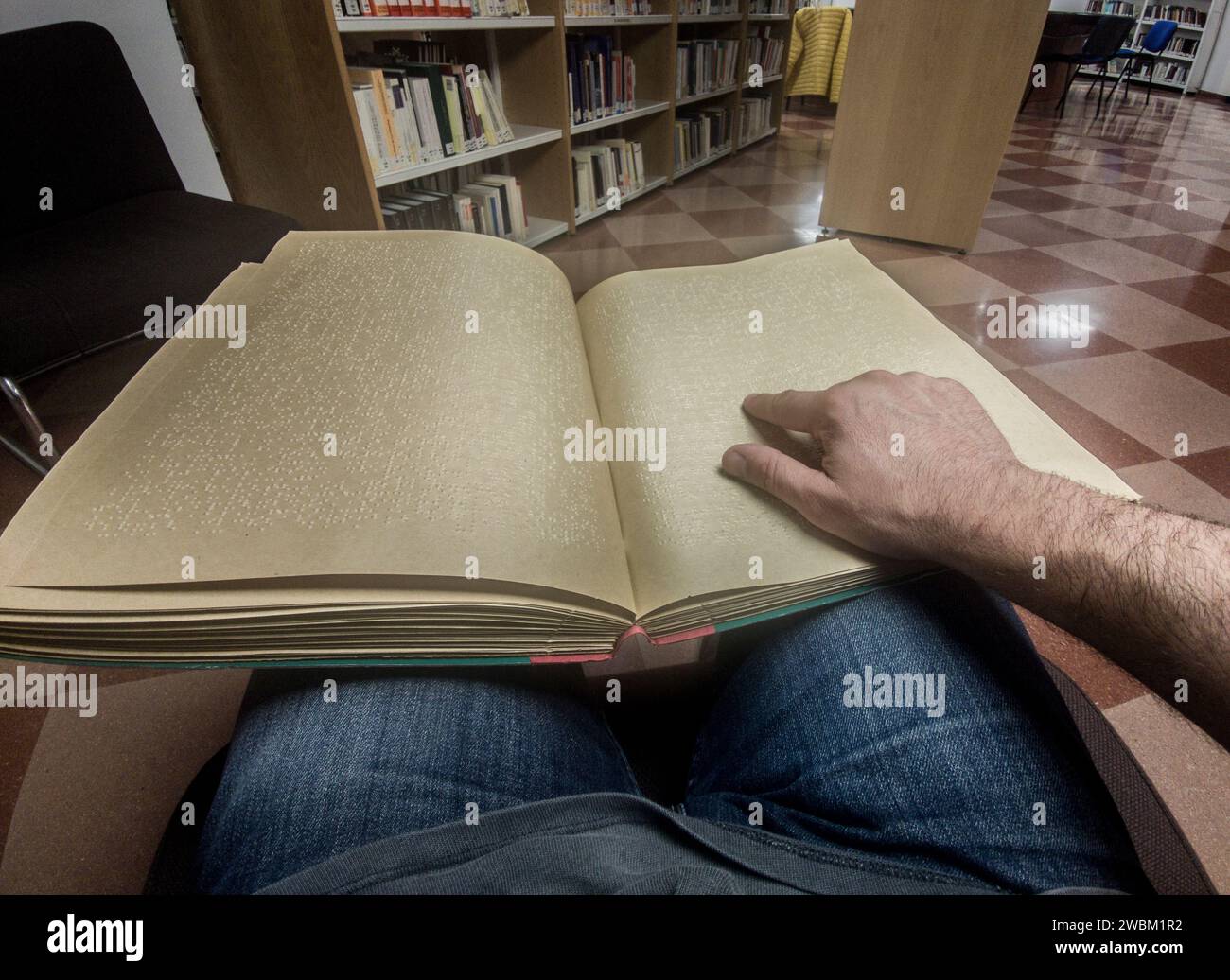 Un uomo cieco che legge un libro in braille in biblioteca. Scatto del punto di vista Foto Stock