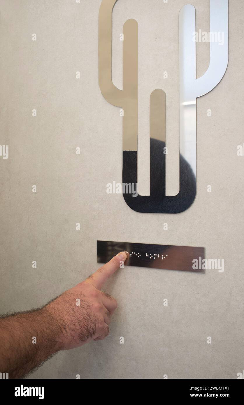 Cartello in braille di lettura maschile cieco sulla porta del gabinetto. Messa a fuoco selettiva Foto Stock