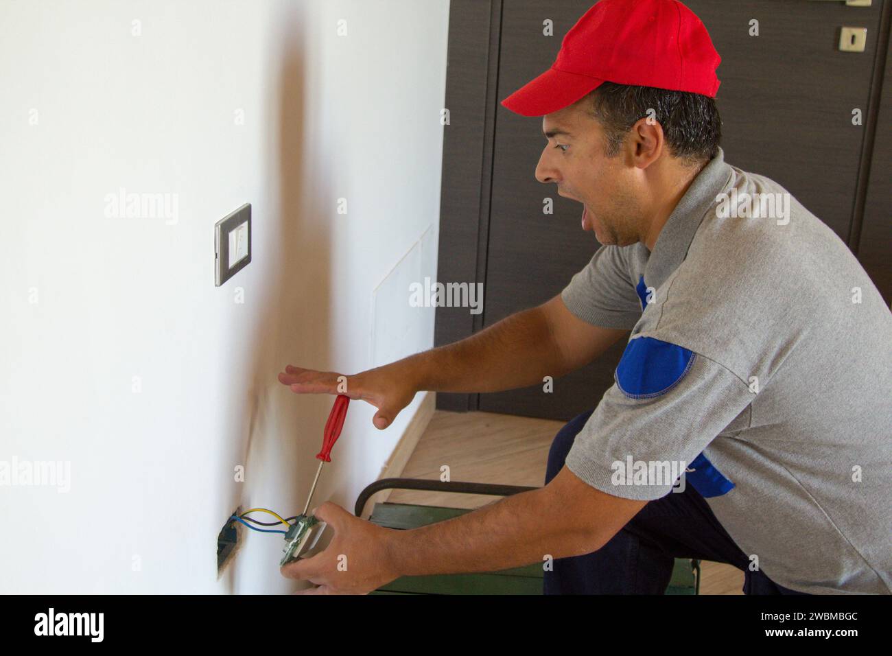 Immagine di un elettricista mentre installa una spina elettrica e riceve una scossa elettrica. Sicurezza del lavoro Foto Stock