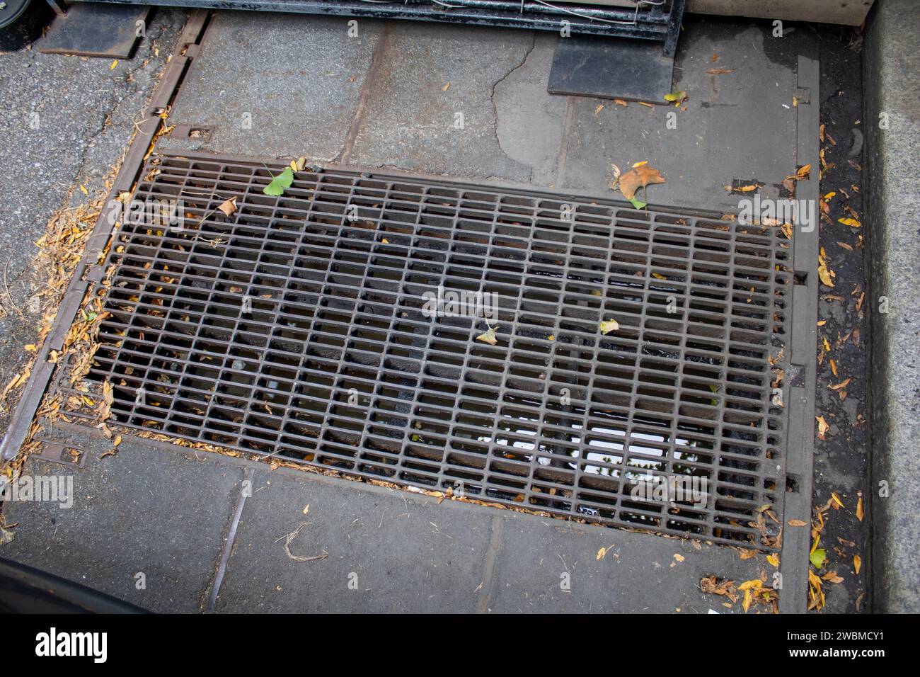 Primo piano di una griglia metallica sul fondo stradale con macchie di ruggine e accumulo di sporcizia visibili Foto Stock