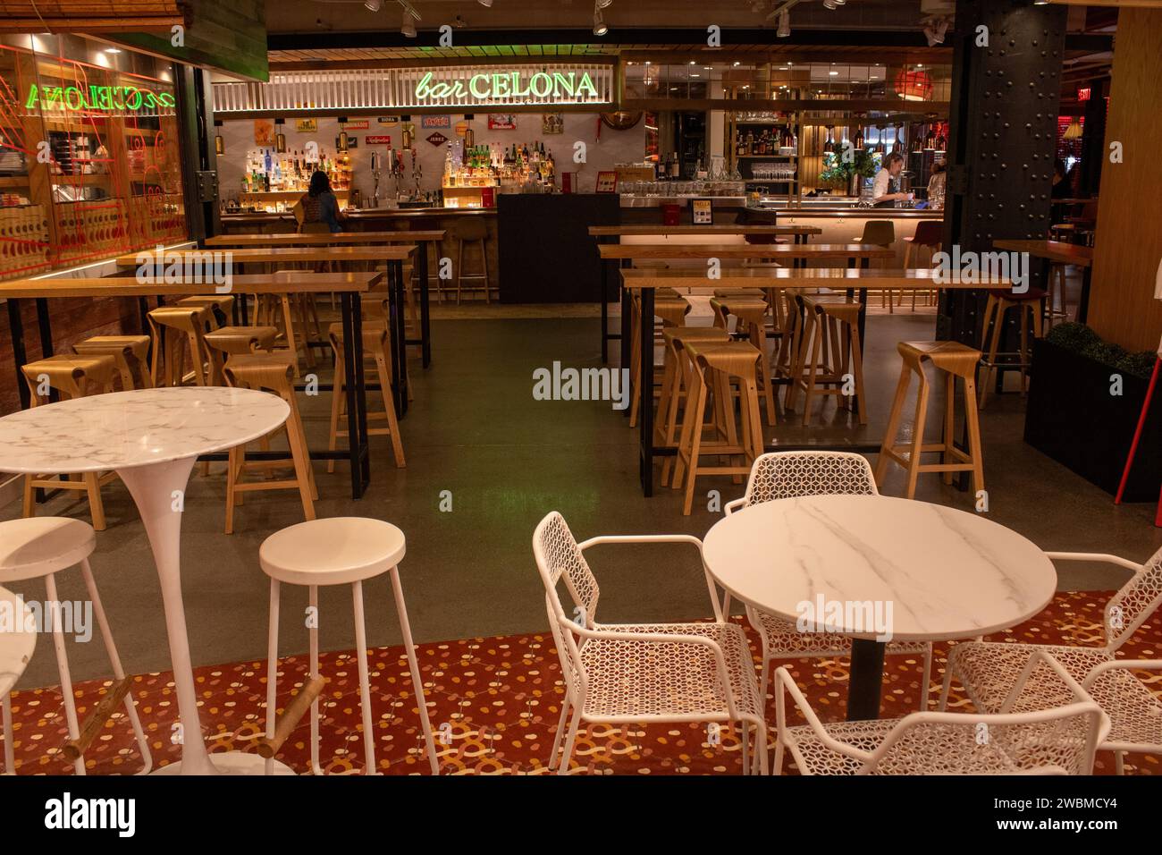 Una sala ben illuminata presenta una varietà di tavoli e sedie in legno ordinatamente disposti in gruppi, perfetti per qualsiasi riunione Foto Stock