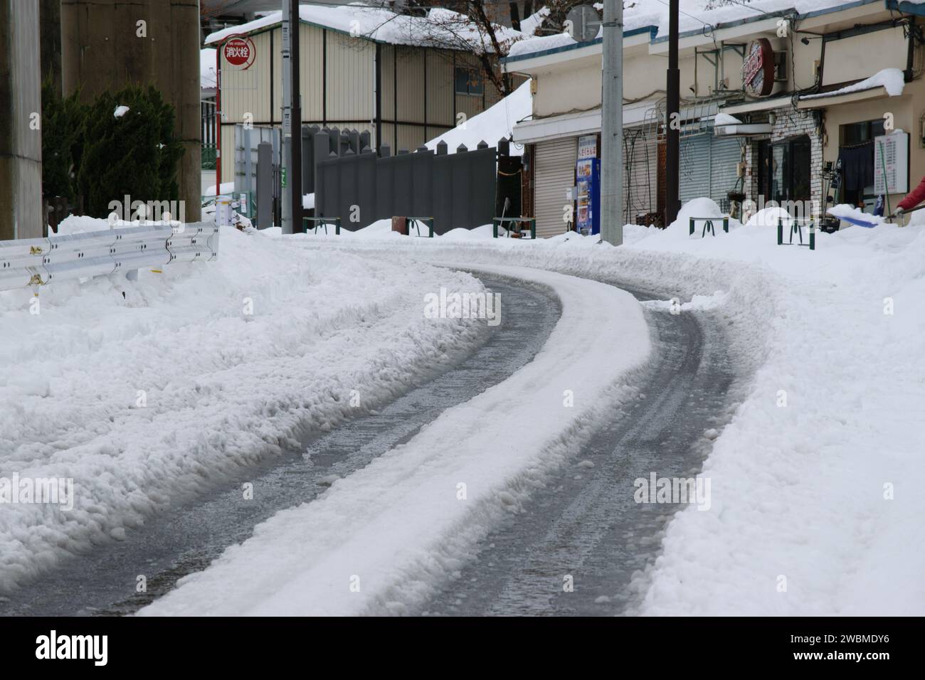 Strada tortuosa ricoperta di neve in una tranquilla area urbana con edifici e banchi di neve ai lati. Foto Stock