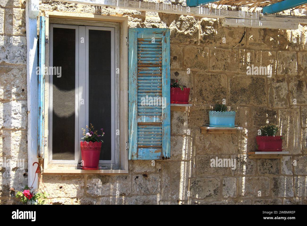 Una stonewall e finestra con persiane in legno blu decorate con vasi di fiori. Foto Stock