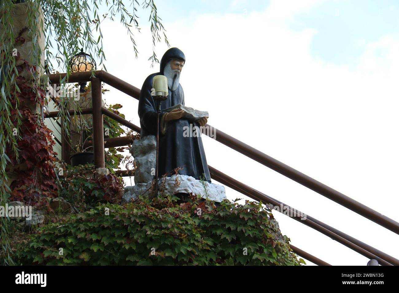 Una statua del libanese saint Mar Charbel sulla cima di una scala di una casa tra il verde. Foto Stock