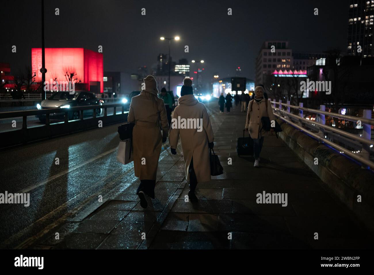 I pendolari tornano a casa in una notte d'inverno attraverso il Waterloo Bridge accanto a un National Theatre illuminato di colore rosso bankside, Southbank, nel centro di Londra, in Inghilterra. Foto Stock