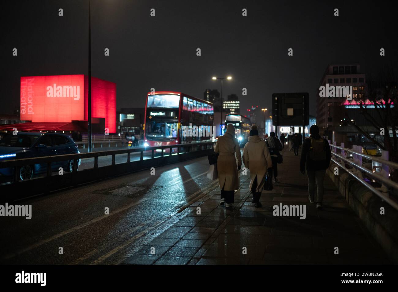 I pendolari tornano a casa in una notte d'inverno attraverso il Waterloo Bridge accanto a un National Theatre illuminato di colore rosso bankside, Southbank, nel centro di Londra, in Inghilterra. Foto Stock