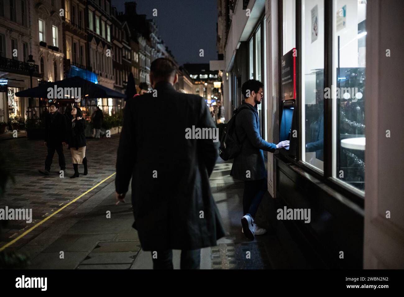 Un uomo effettua un prelievo di contanti da un bancomat in una serata d'inverno buia nella zona di Covent Garden nel West End di Londra, Inghilterra, Regno Unito Foto Stock