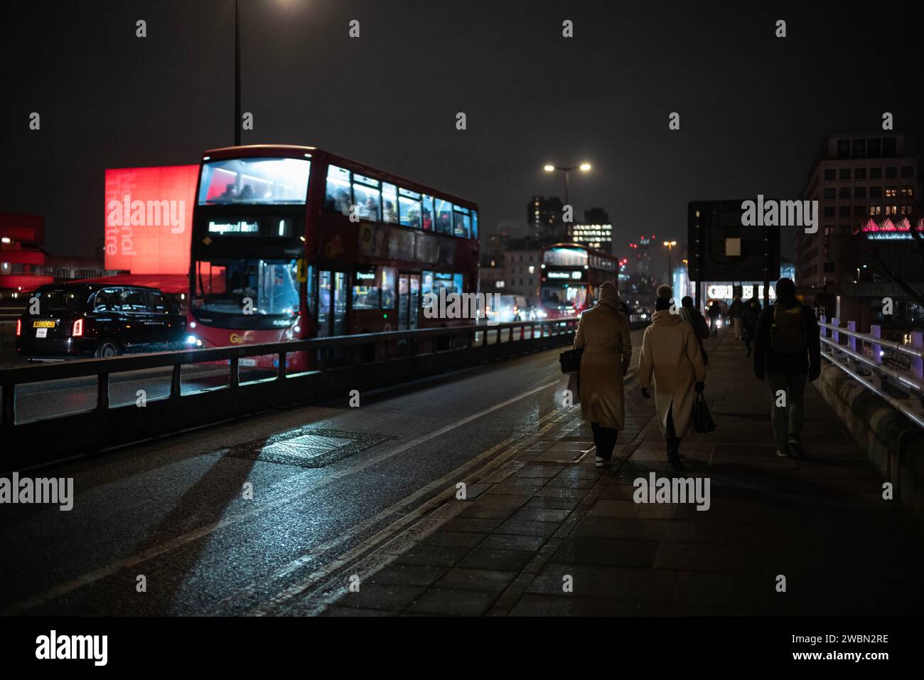 I pendolari tornano a casa in una notte d'inverno attraverso il Waterloo Bridge accanto a un National Theatre illuminato di colore rosso bankside, Southbank, nel centro di Londra, in Inghilterra. Foto Stock
