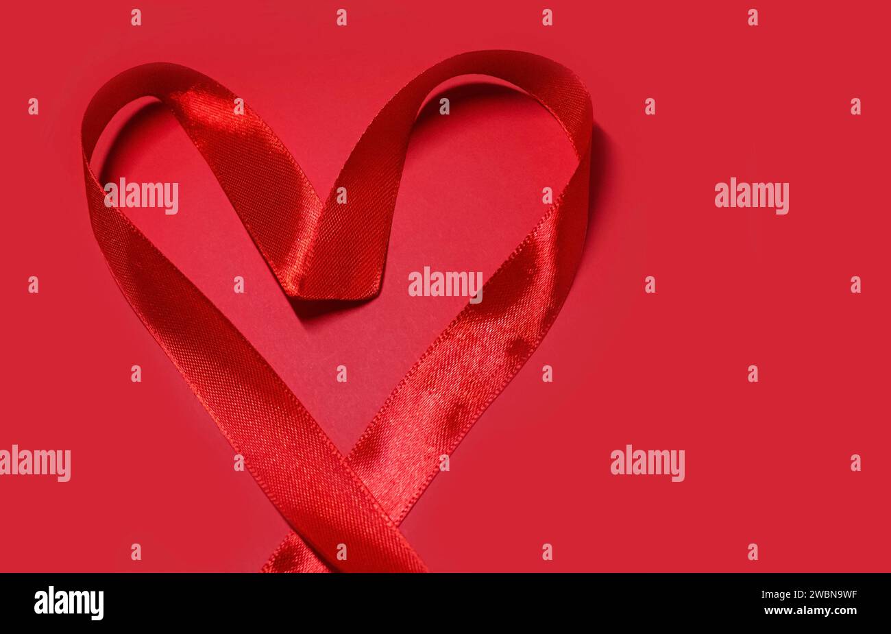 Forma a cuore rosso dal nastro satinato San Valentino su sfondo rosso con spazio per la copia. Concetto per beneficenza, assicurazione sanitaria, amore, cardiolo internazionale Foto Stock