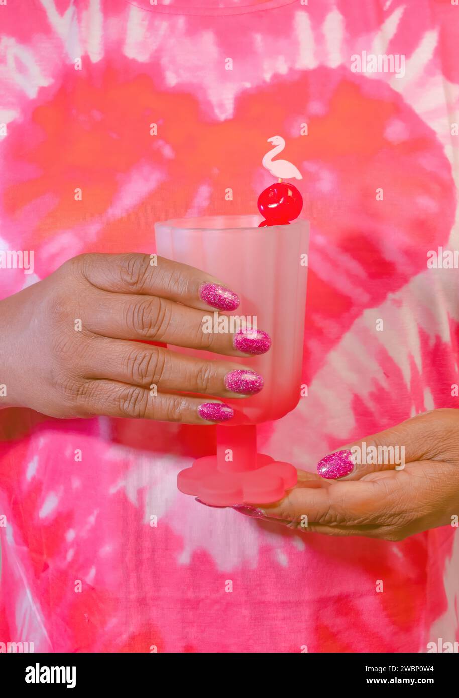 Una donna afro-americana che tiene un cocktail con un Flamingo Swizzle Stick Foto Stock