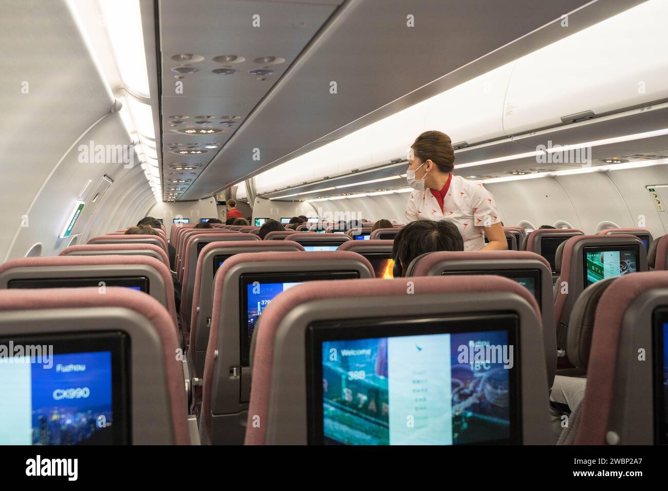 Vista dell'interno di un aereo dove una hostess si trovava nella corsia rispondendo a una richiesta di un passeggero, Hong Kong Cina. Foto Stock