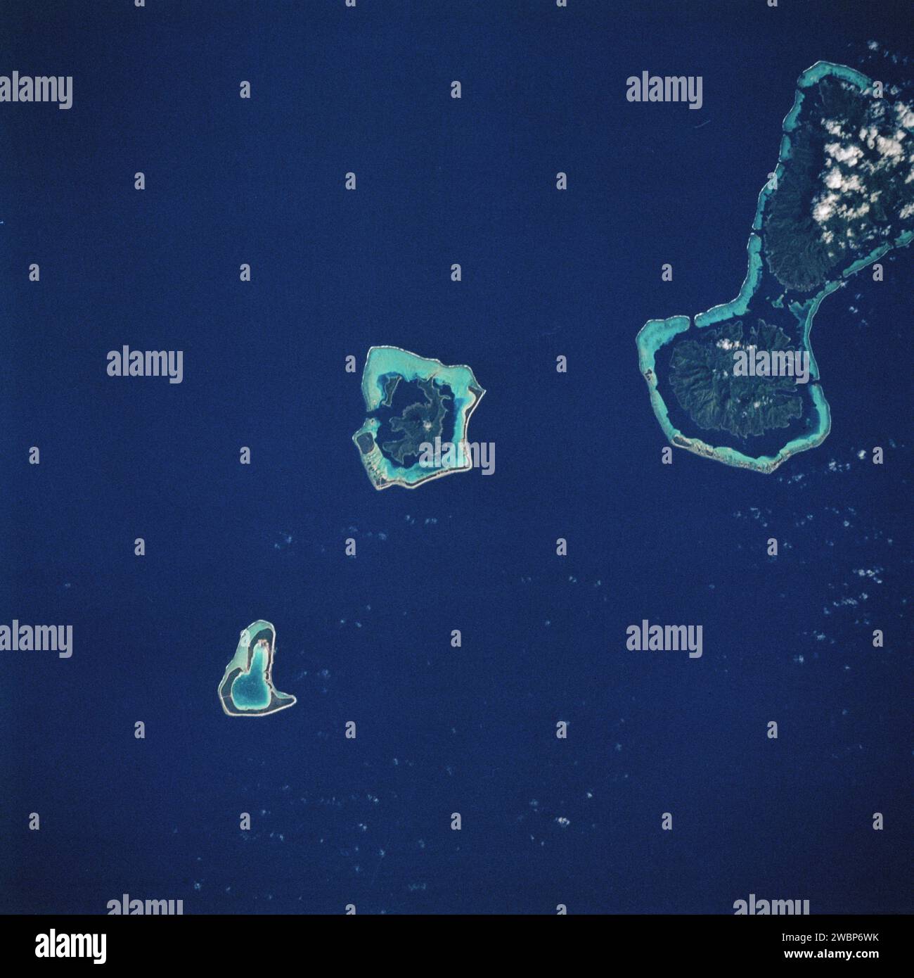 Bora-Bora e la sua ampia barriera corallina sono fotografati dallo Space Shuttle Challenger sulle Isole Society, con Raiatea e Tahaa visibili. Le isole vulcaniche lentamente si abbassano nella crosta oceanica, mentre i coralli mantengono la piattaforma della barriera corallina. Foto Stock