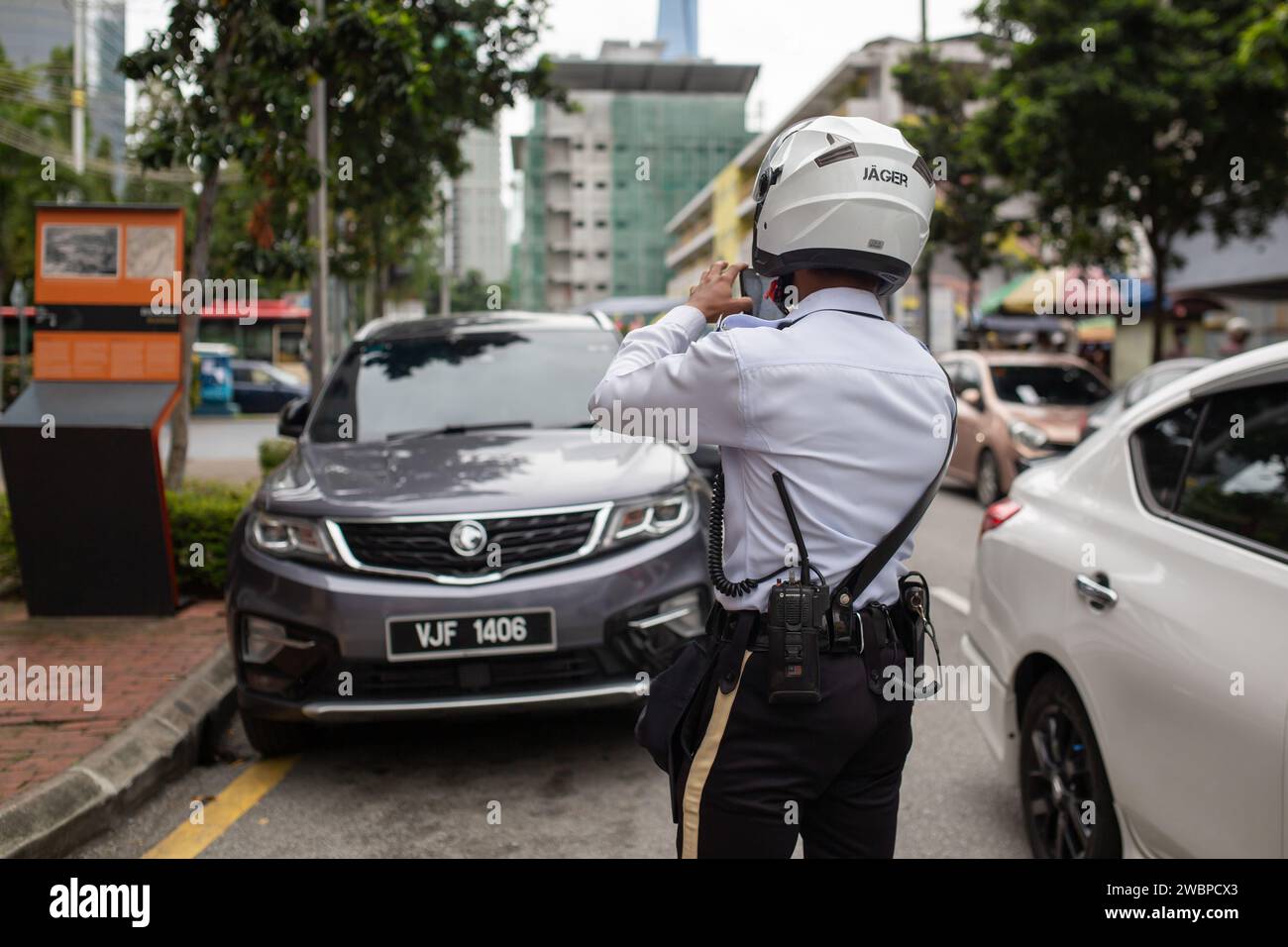 Kuala Lumpur, Malesia - 8 gennaio 2024: Agente della polizia stradale che fotografa ed emette biglietti per i proprietari di veicoli parcheggiati illegalmente. Foto Stock