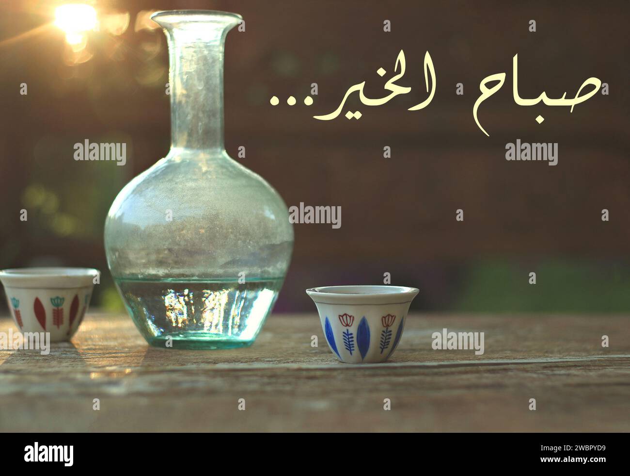 Buon giorno scritto in arabo. Due tazze di caffè tradizionali libanesi insieme a una caraffa d'acqua in vetro, ebrik. Foto Stock