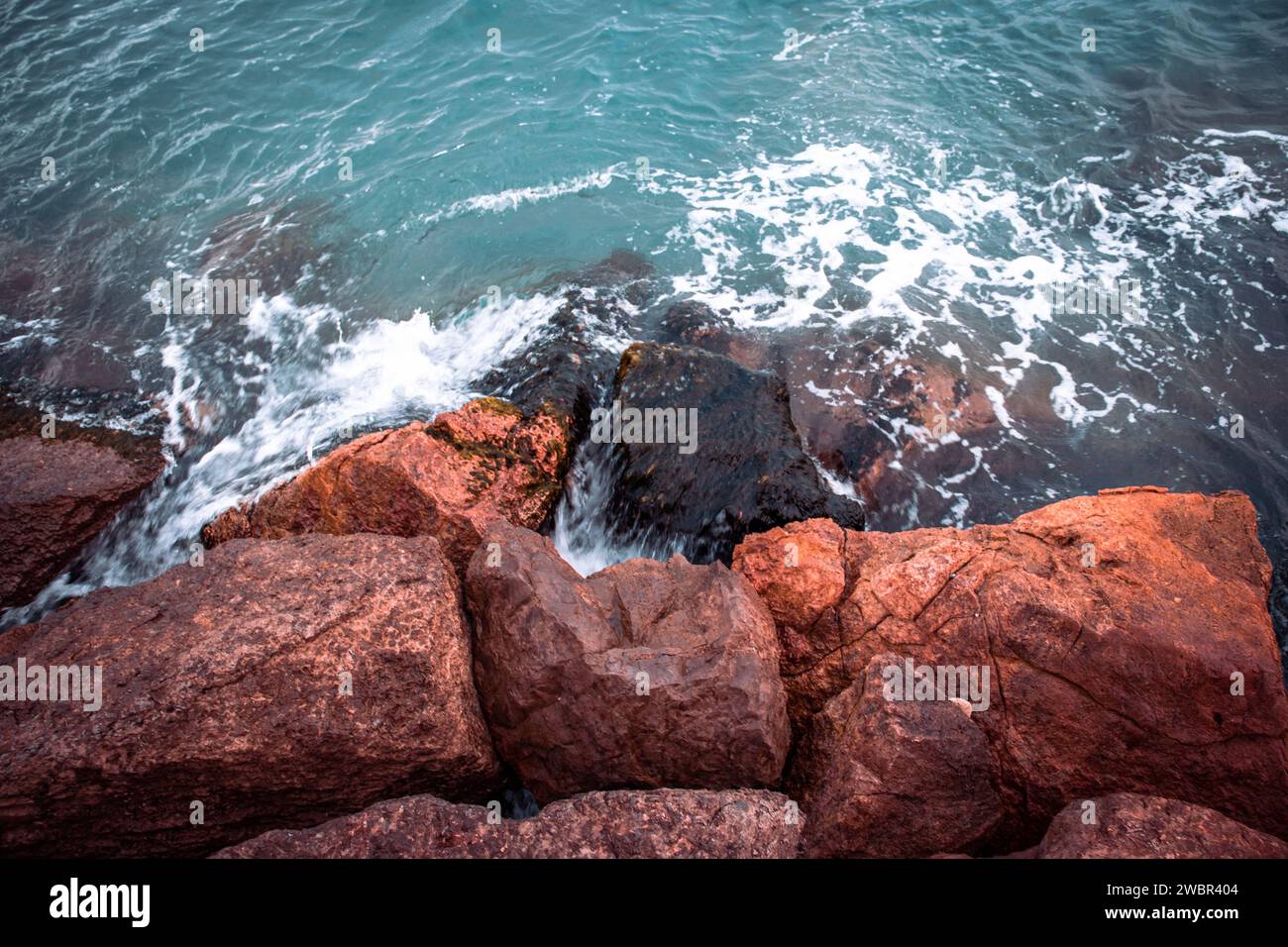 Mare tempestoso d'inverno mediterraneo. Primo piano sull'acqua con le pietre sulla foto del concept della spiaggia. Foto Stock