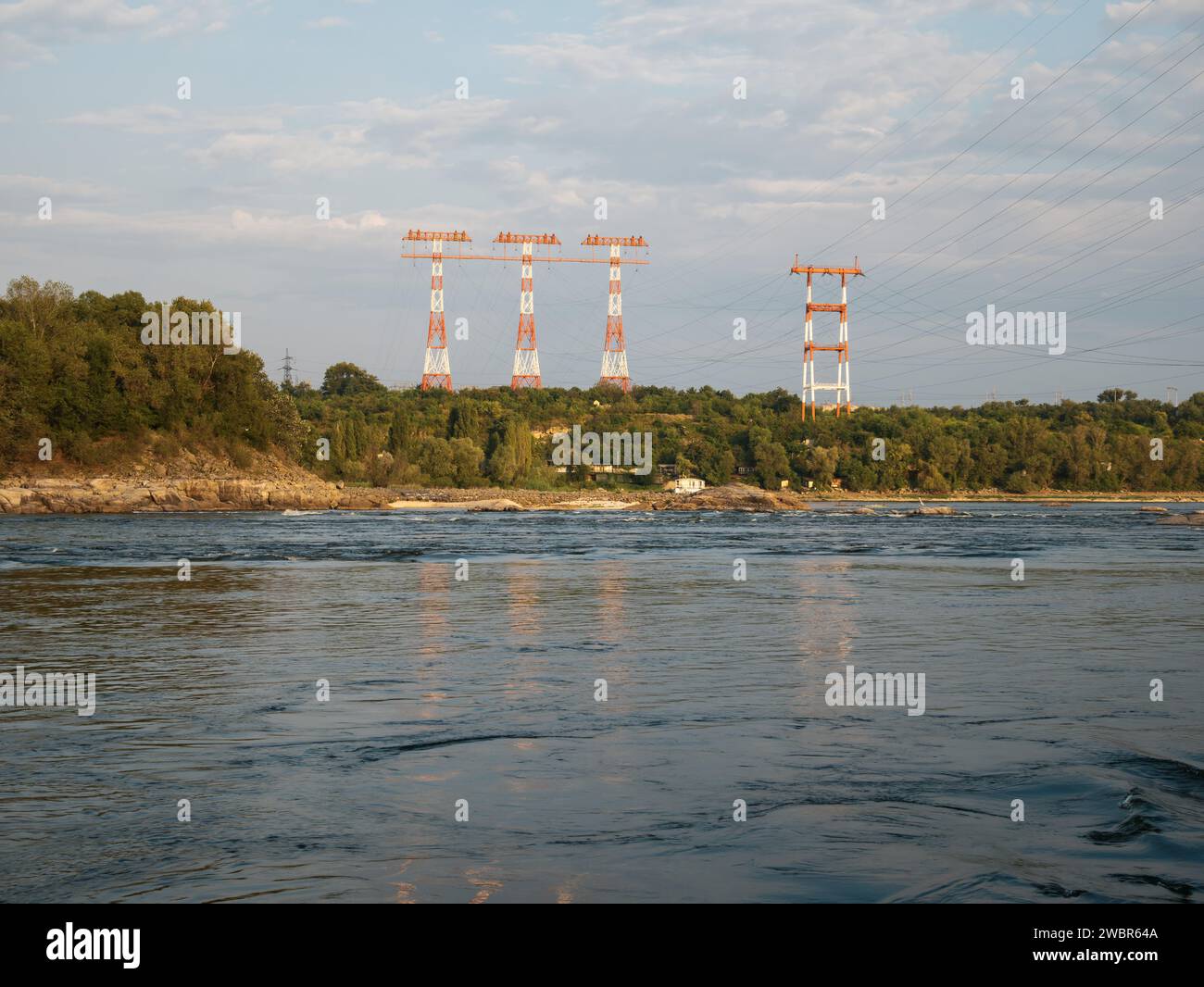 Enormi alberi di trasmissione di potenza che torreggiano sopra la foresta e un ampio fiume con sponde rocciose Foto Stock