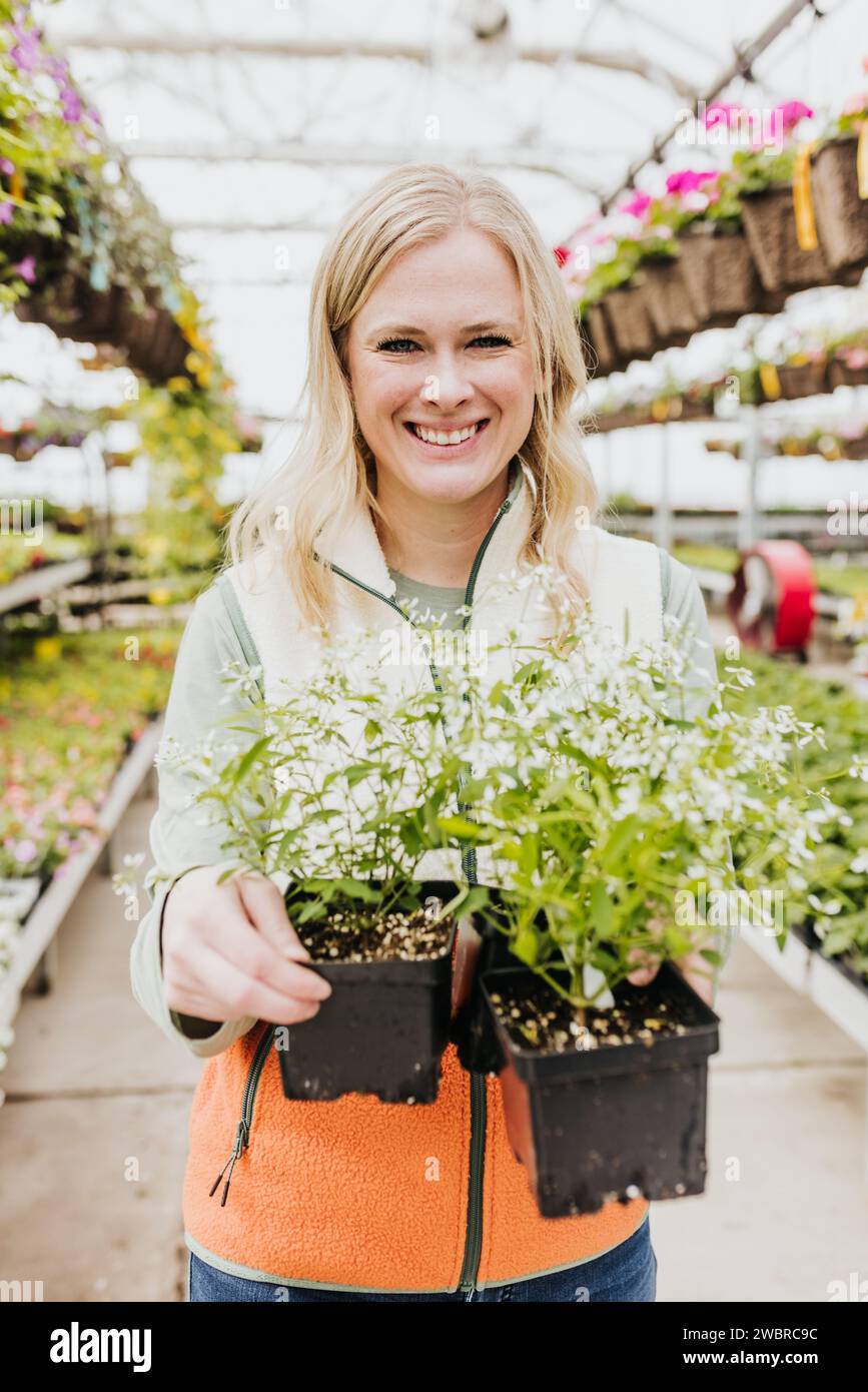 La donna guarda la macchina fotografica mentre tiene fiori bianchi alla serra Foto Stock