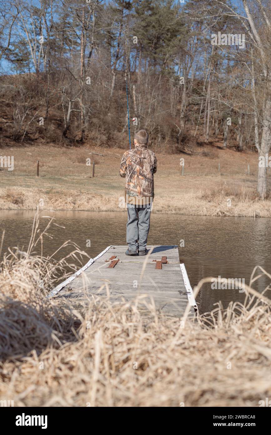 Schiena di un ragazzo che lancia canna da pesca dal molo nello stagno Foto Stock