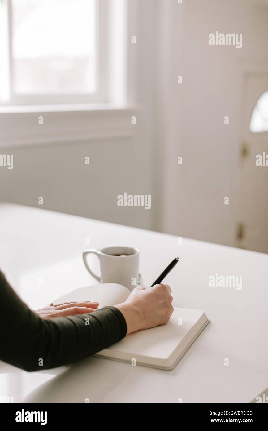 cucina bianca minimalista con donna che scrive su un diario Foto Stock