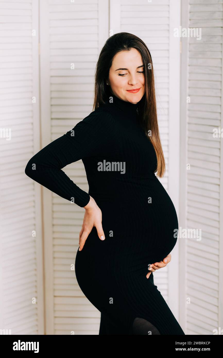 Elegante aspettativa: Un profilo di forza e Grazia. Donna incinta in un vestito stretto nero. Bella silhouette Foto Stock