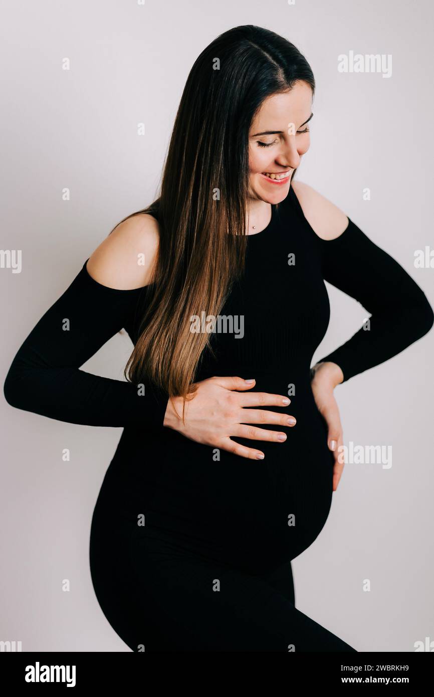 Elegante aspettativa: Un profilo di forza e Grazia. Donna incinta in un vestito stretto nero. Bella silhouette Foto Stock