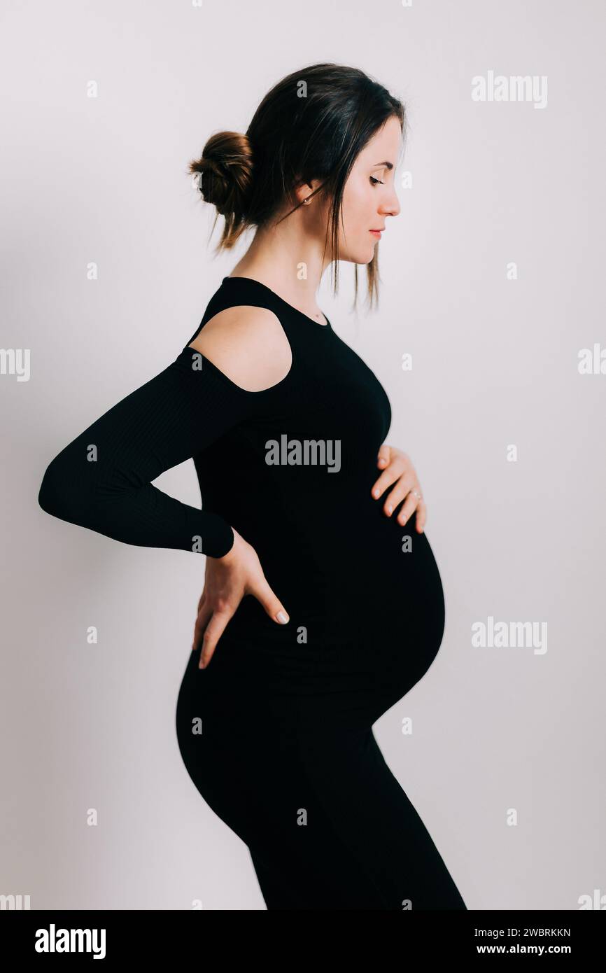 Elegante aspettativa: Un profilo di forza e Grazia. Donna incinta in un vestito stretto nero. Bella silhouette Foto Stock