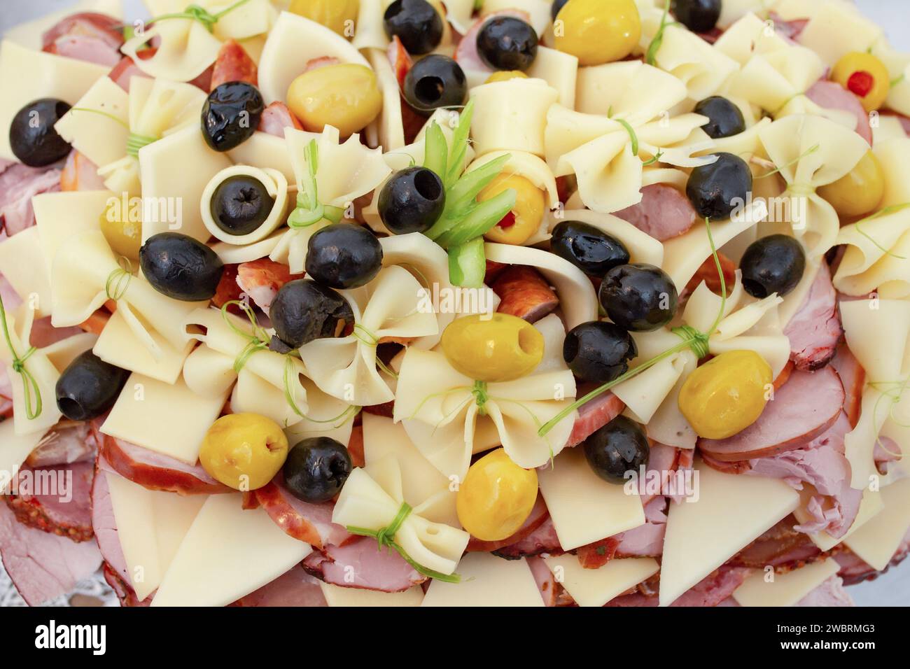 vari prodotti a base di carne e fette di formaggio stagionato disposte, impilate su un piatto con olive nere, sfondo per antipasti Foto Stock
