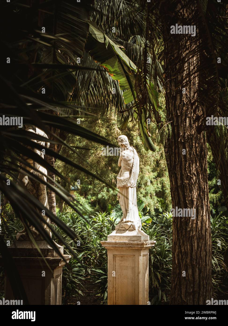 Statua classica nel parco pubblico Parque de Málaga, giardino botanico a Malaga, Andalusia, Spagna, giardino tropicale mediterraneo con pini e palme Foto Stock