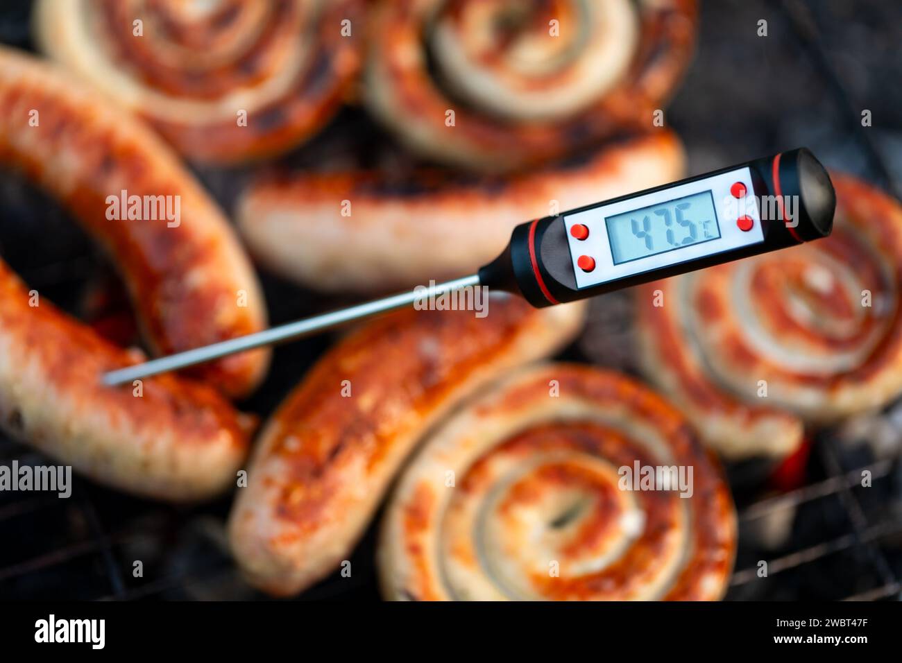 Primo piano di un termometro digitale per la carne che visualizza la temperatura al di sotto della soglia di cottura sicura per le salsicce grigliate, segnalando una potenziale guarigione Foto Stock