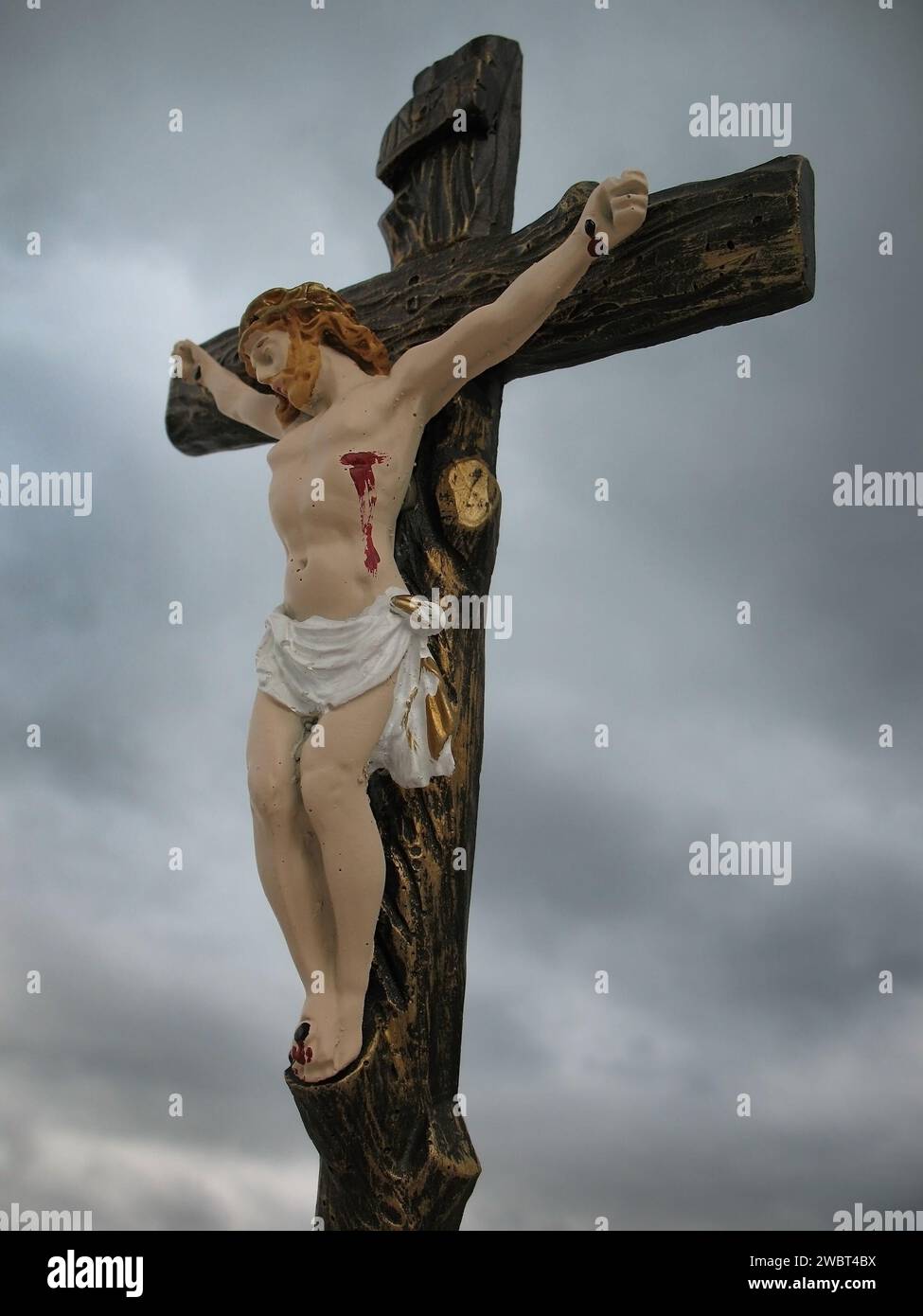 Statuetta di Gesù crocifisso contro un cielo cupo e nuvoloso. Foto Stock