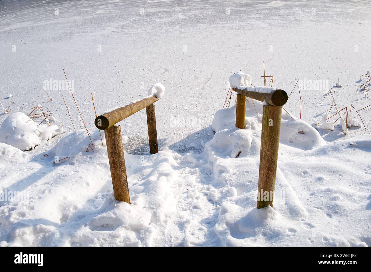 Corrimano di legno tra terra e acqua ghiacciata del lago nella foresta sotto la neve Foto Stock