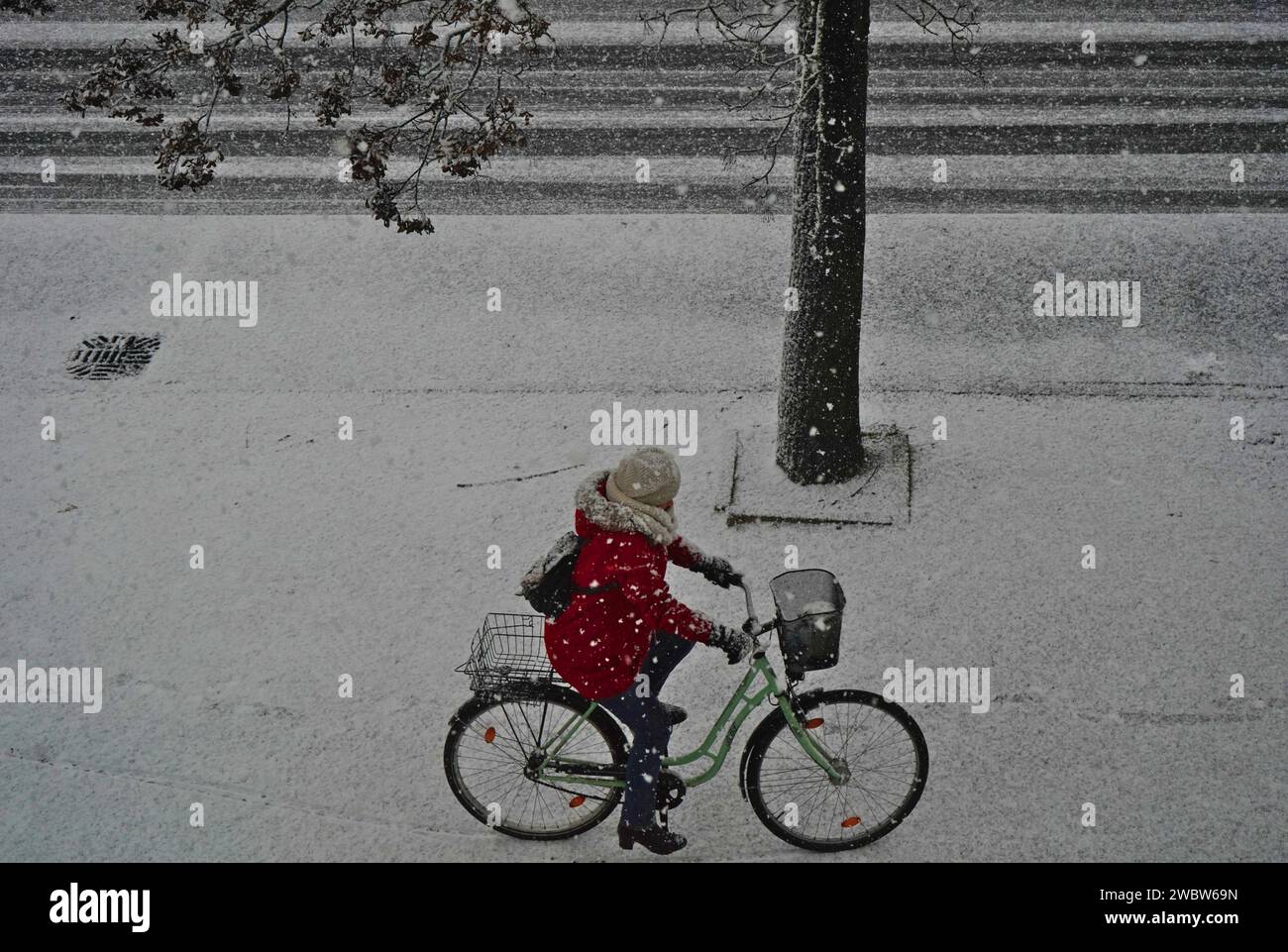 Eleganza invernale: Un ciclista con rivestimento rosso che corre sulle strade innevate di una città della Germania Est nello stato del Brandeburgo Foto Stock