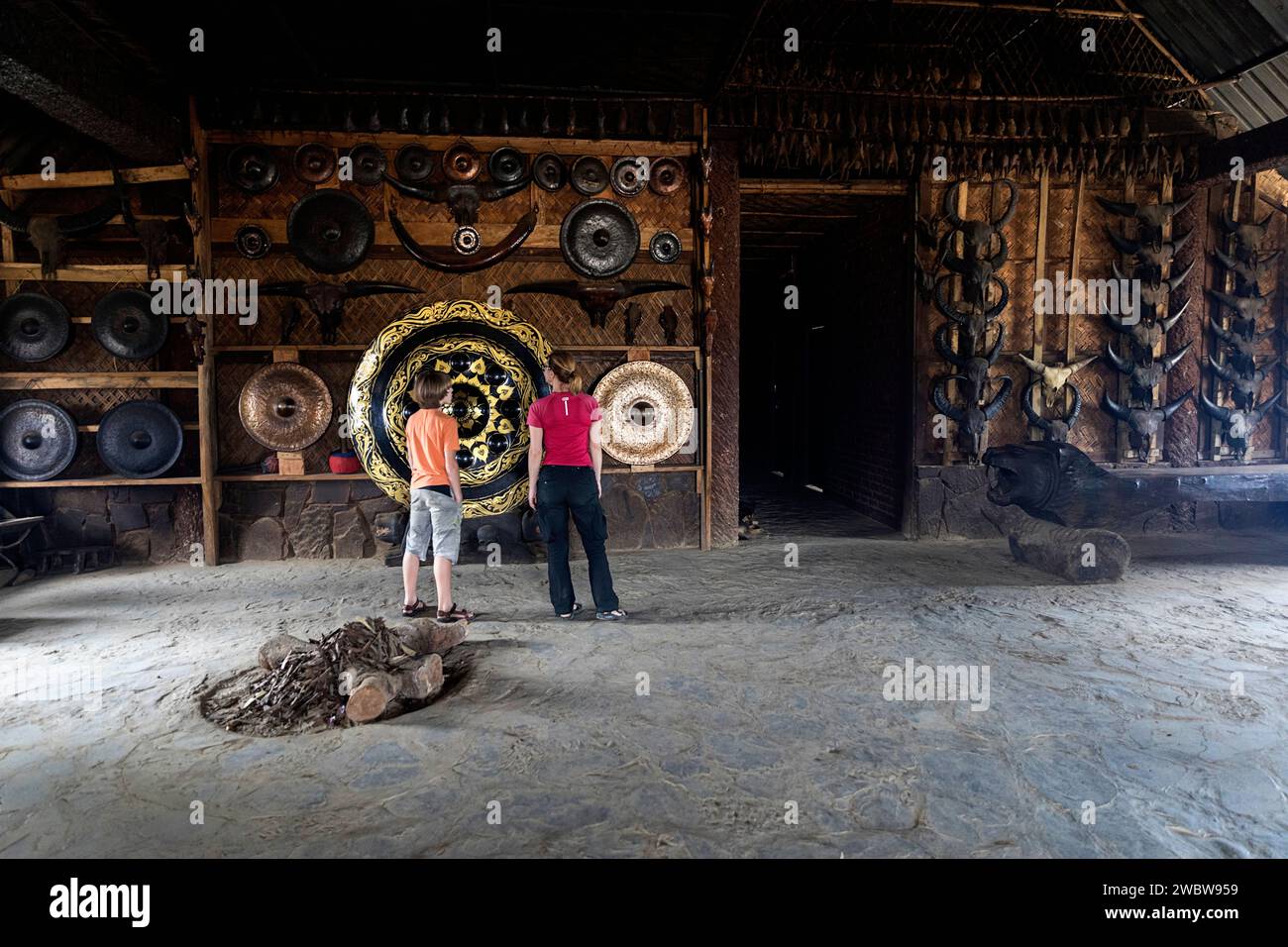 Turisti che guardano le opere d'arte tribali realizzate dai membri della tribù konyak all'ingresso della lunga casa konyak nel villaggio di longwa, nagaland, india Foto Stock