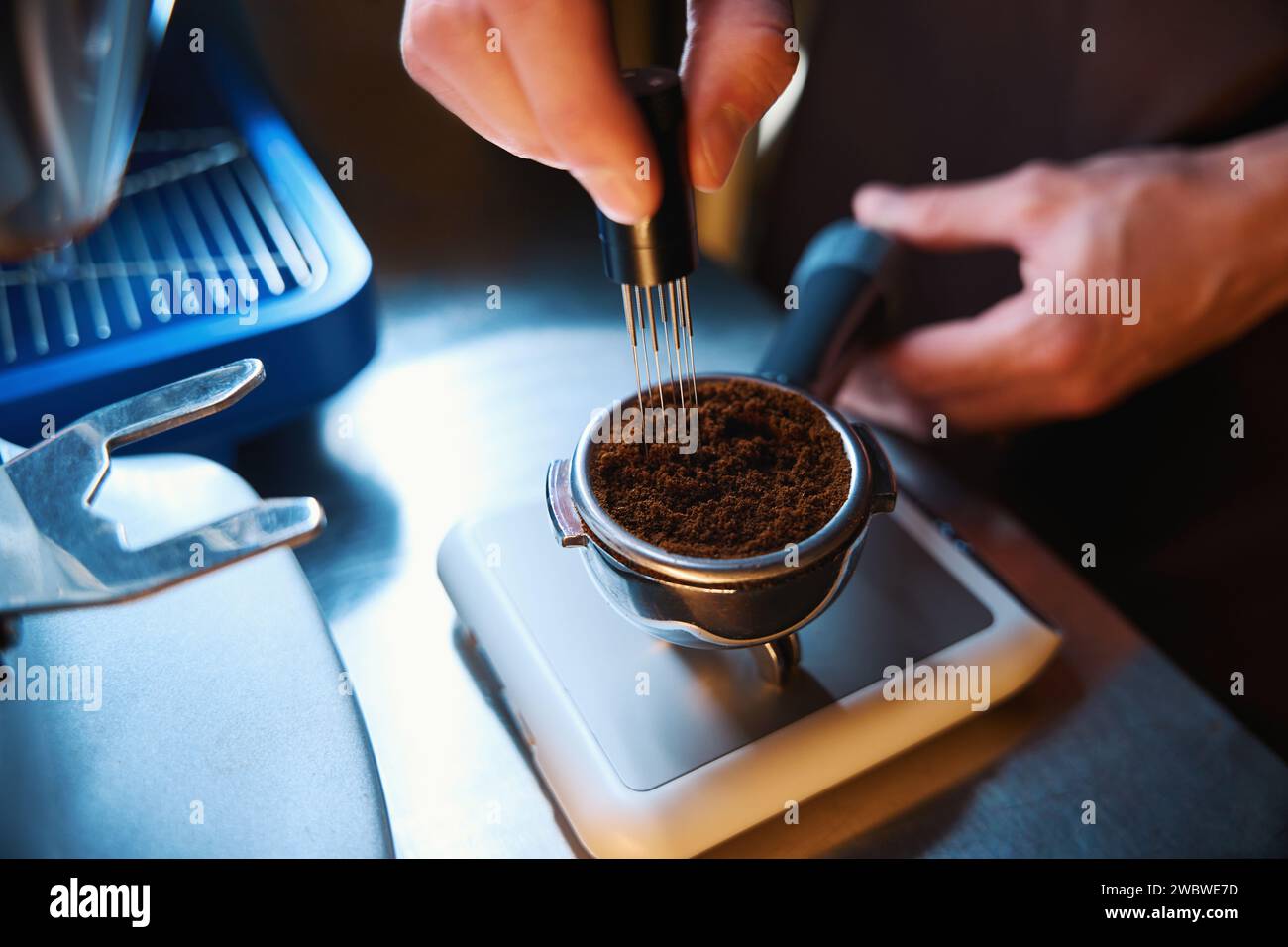 Il barista ha le mani per livellare il caffè nel portafiltro utilizzando lo strumento di distribuzione delle polveri Foto Stock