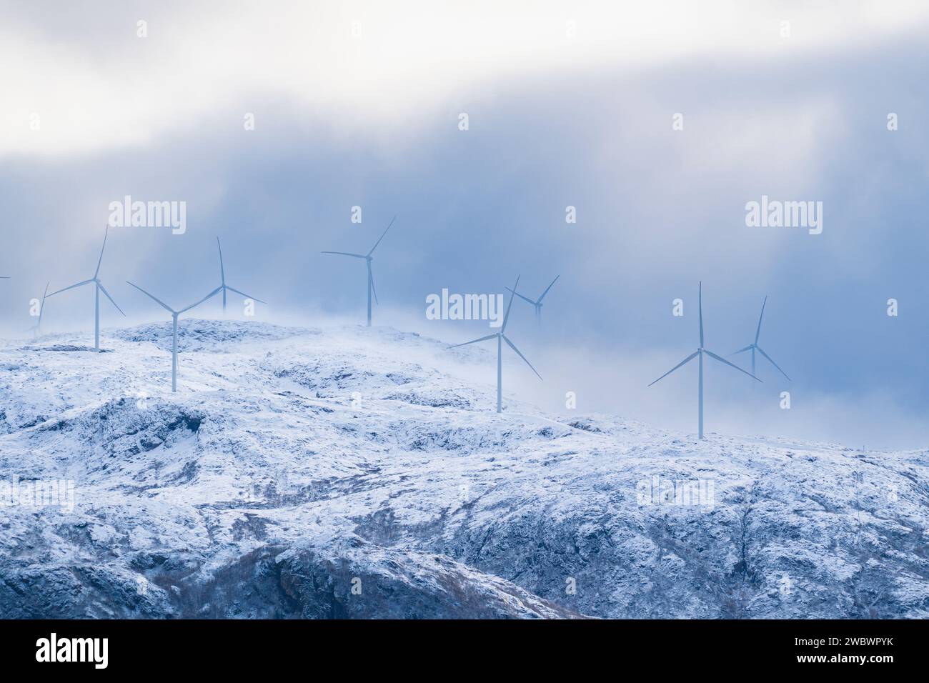 Mulini a vento sulla costa dell'Atlantico in ogni condizione atmosferica. Vista sulle montagne innevate dall'isola di Kvaløya, Norvegia, con molte turbine eoliche Foto Stock