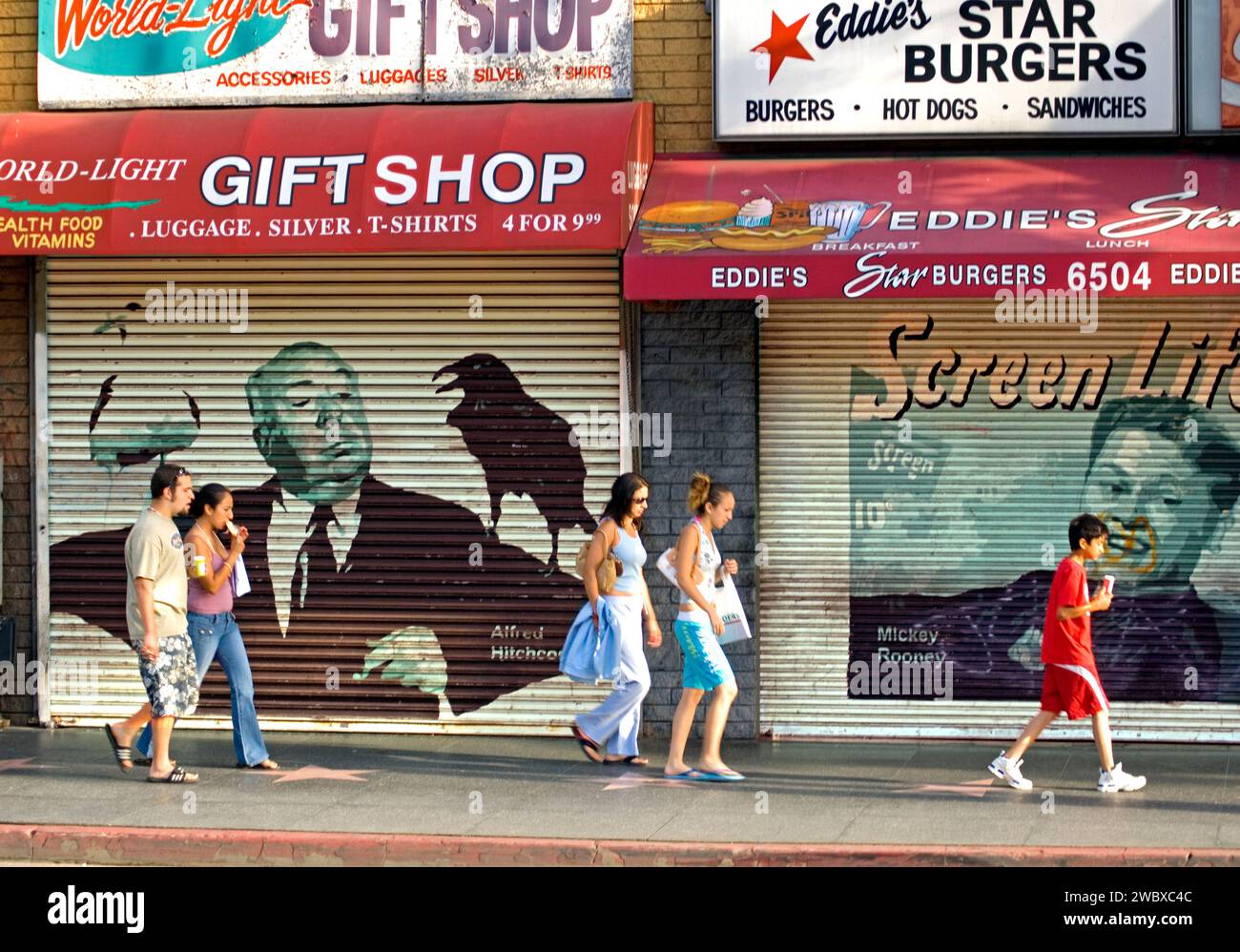 I turisti camminano davanti alle immagini delle icone di Hollywood dipinte sulle persiane del negozio su Hollywood Blvd., LosAngeles, CA, USA Foto Stock