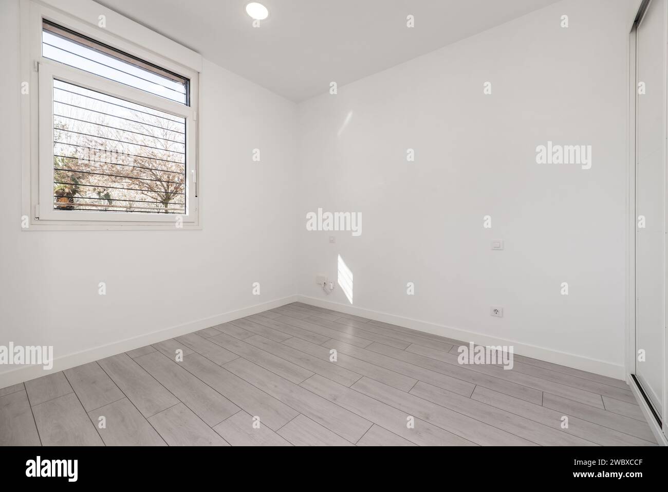 Camera vuota in una casa tipo loft al piano terra con armadio a muro con porte scorrevoli, pavimenti dai colori chiari e finestre in alluminio Foto Stock