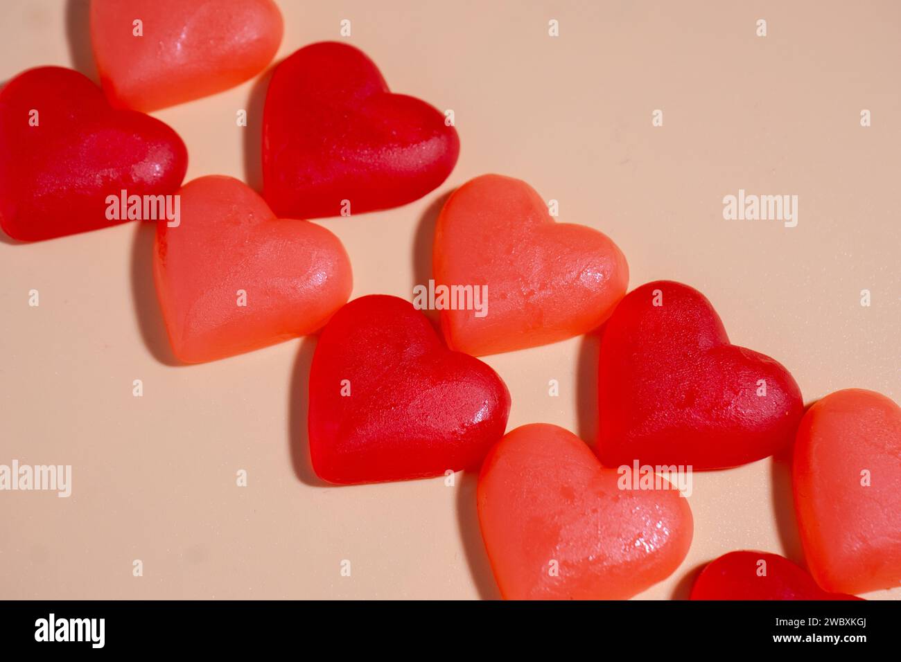 Serie di due linee di caramelle rosse e pesche a forma di cuore su sfondo arancione pastello, disposte in diagonale in un'immagine orizzontale con aspro li Foto Stock