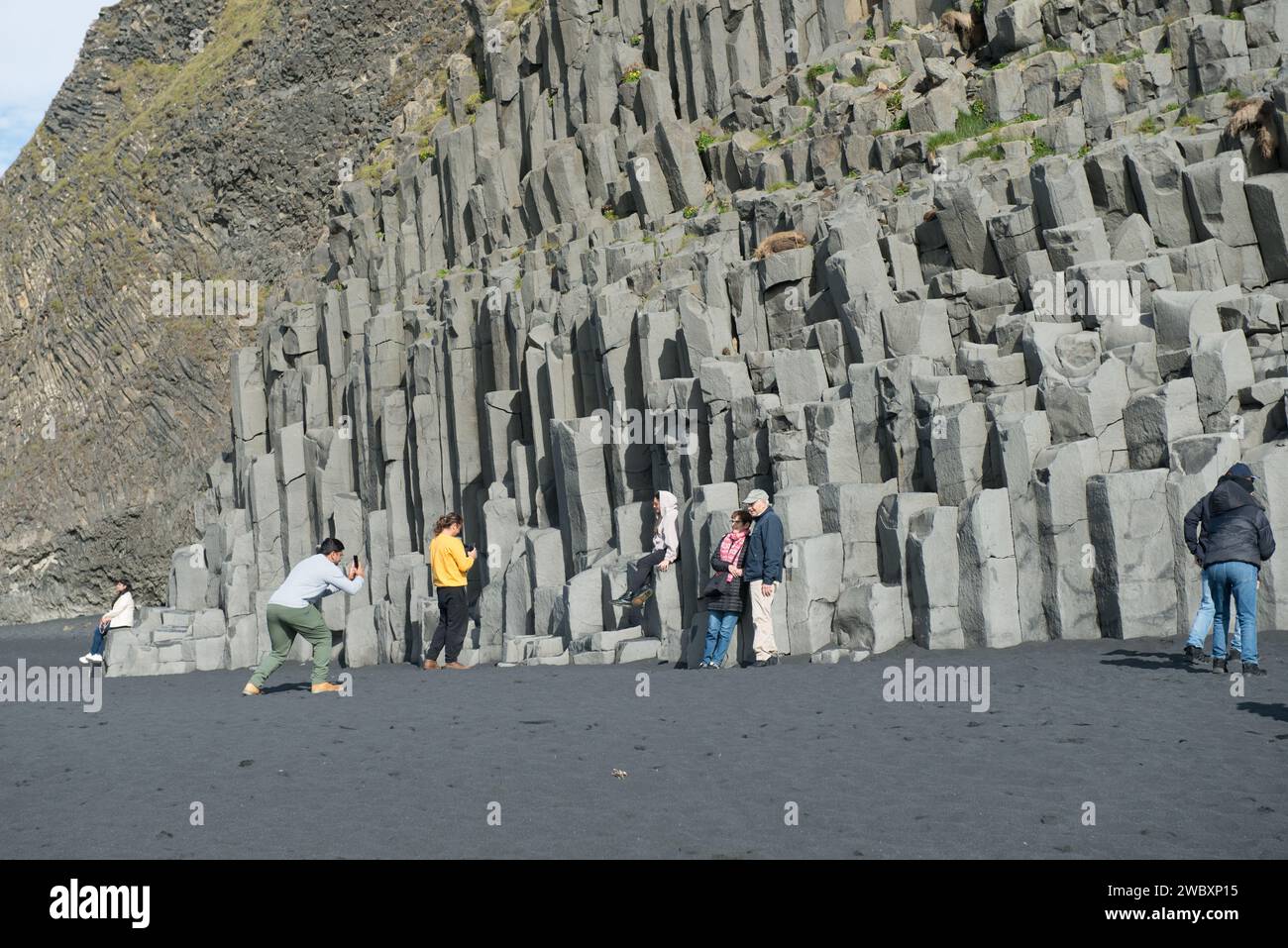 I turisti in posa per foto sulle colonne di Basalt di Reynisfjall, una montagna di tufo alta 340 metri vicino alla città di Vik, Islanda Foto Stock