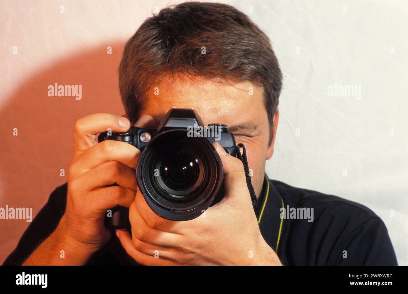 fotografo con fotocamera che scatta una foto, un ritratto, una fotocamera davanti al volto, guardando attraverso la fotocamera Foto Stock
