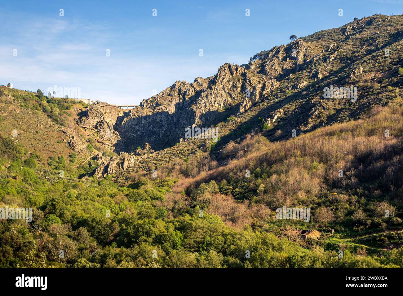Paesaggio montano roccioso con una valle boscosa e la diga di Caldeirão sullo sfondo, nel Parco naturale della Serra da Estrela in Portogallo. Foto Stock