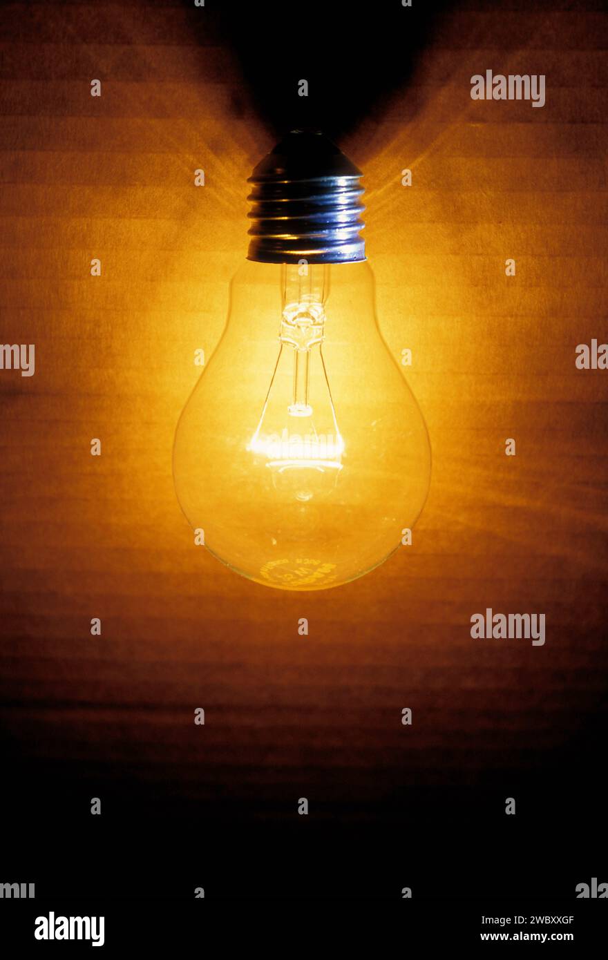 primo piano di una vecchia lampadina accesa, di una scatola quando lo sfondo è illuminato, illuminata da una luce calda gialla o arancione Foto Stock