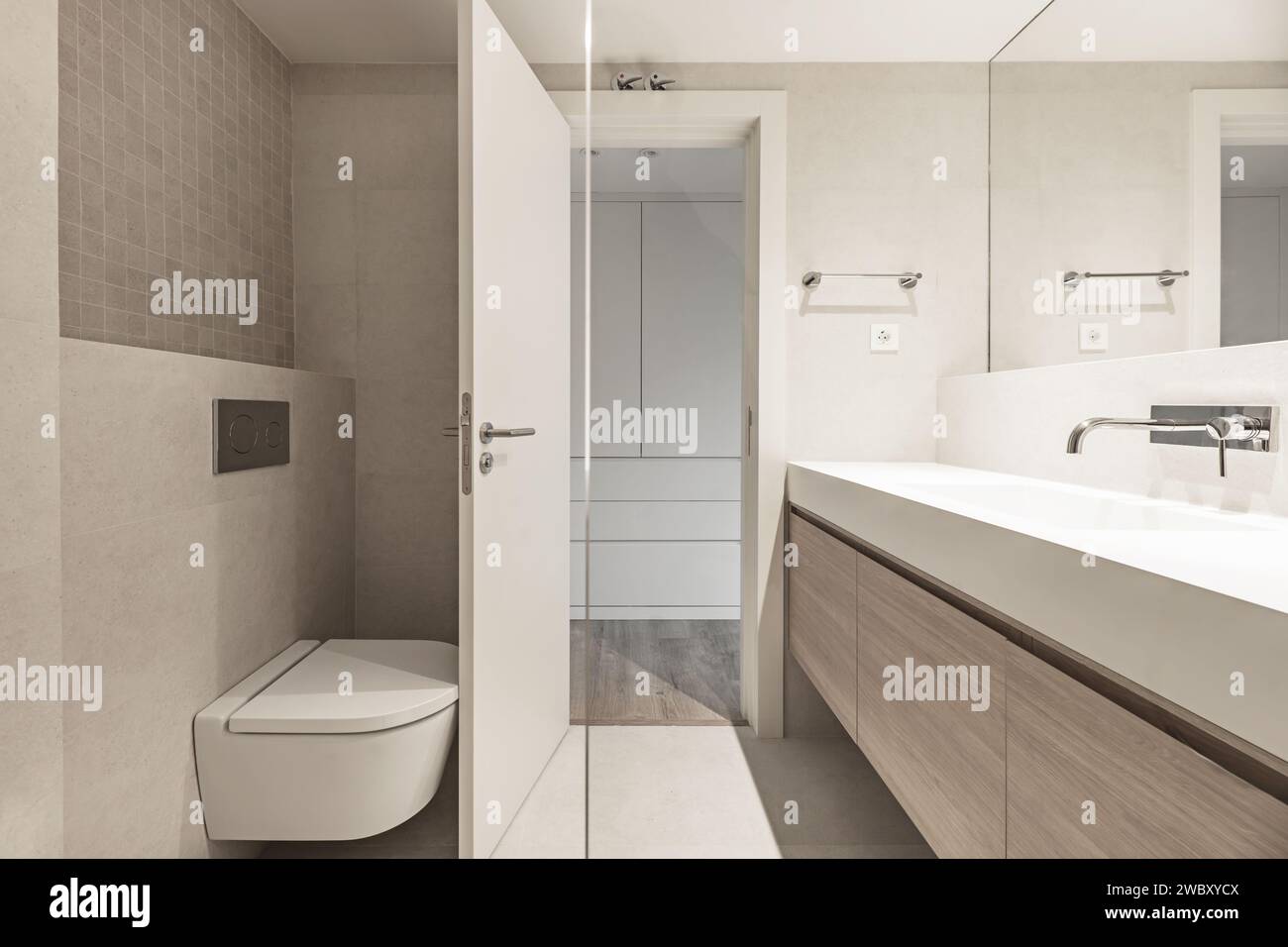 Un piccolo bagno con pareti piastrellate con effetto marmo solare, specchio a parete integrato e lavabo monopezzo con rubinetto cromato. Foto Stock