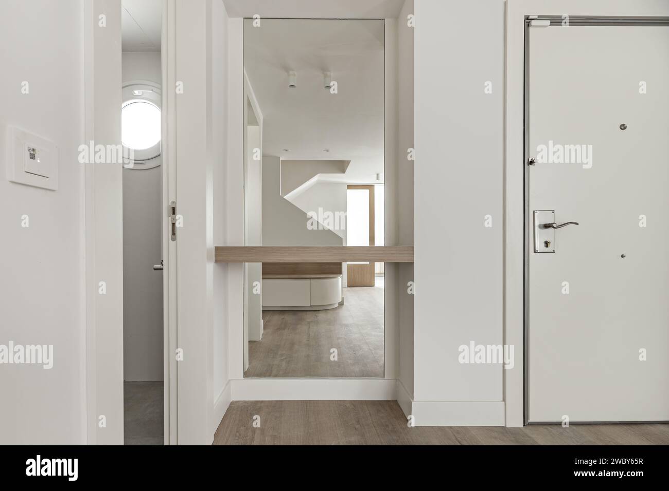 Lobby di una casa con pareti dipinte di bianco liscio, uno specchio a figura intera accanto alla porta d'ingresso, guardaroba bianco a incasso, scala, legno coordinato Foto Stock